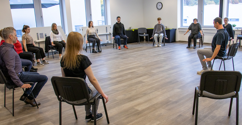 KLEIN Mitarbeitende in Stuhlkreis nehmen an Übungen von Physio Luis Otero teil