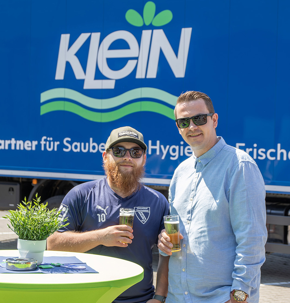 Zwei Teilnehmende stehen mit Getränken an einem Stehtisch vor einem KLEIN LKW beim Sommerfest 2026 auf dem Firmengelände in Wilnsdorf.